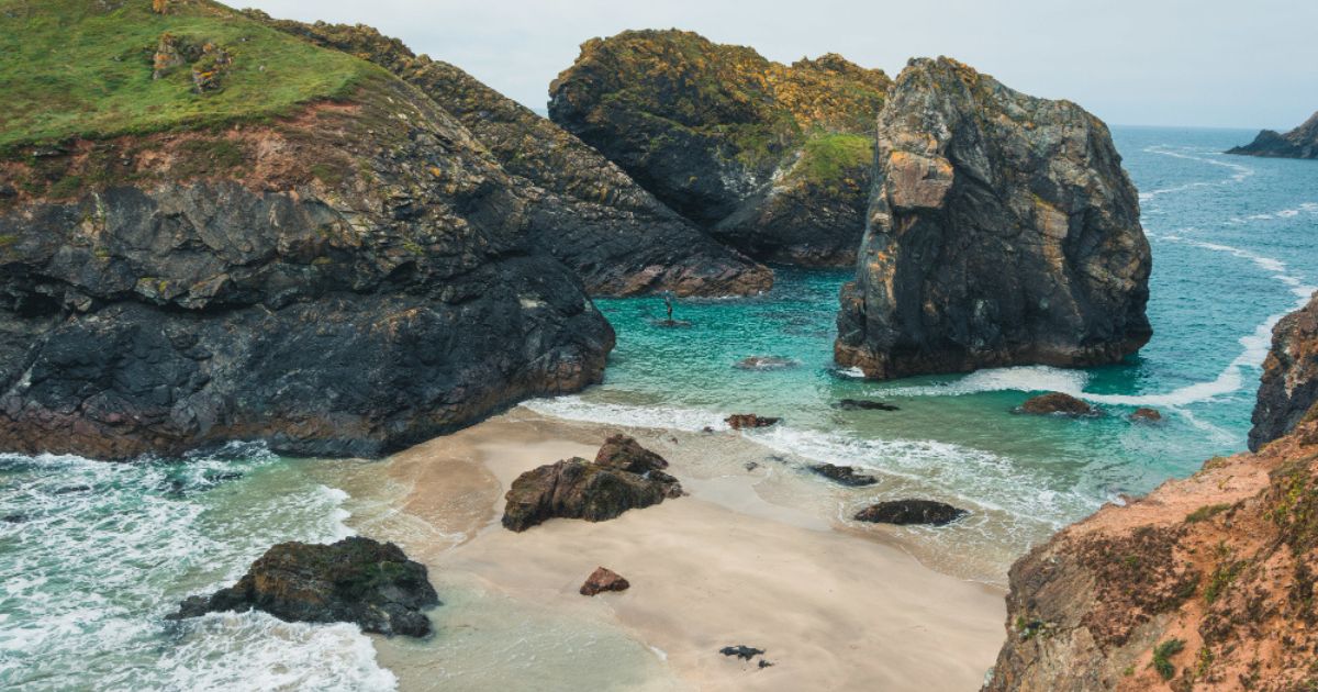 Kynance Cove beach in Cornwall featuring turquoise water, dramatic rock formations, golden sand, and stunning coastal scenery.