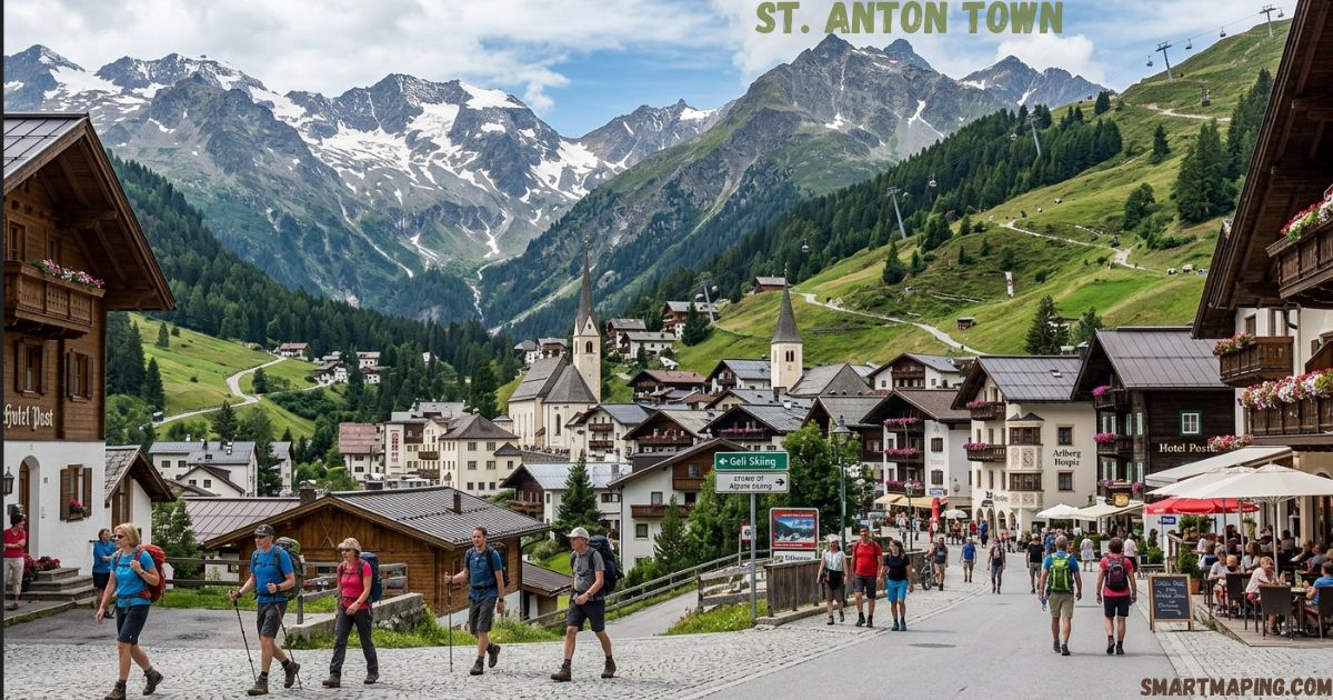 Lush green summer view of St. Anton  Town Alpine village, featuring traditional chalets, church steeples, hikers, and dramatic mountain peaks in the background.