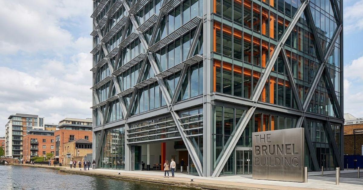 Exterior view of the Brunel Building with its prominent steel diagrid exoskeleton, large glass façade, signature orange structural details, and adjacent canal towpath.