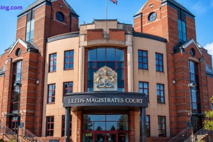 Leeds Magistrates Court ki mukammal imarat ka view, jis mein brick facade, bada glass entrance aur baradari nishan (Royal Coat of Arms) dikhai de raha hai. Ye image Leeds mein qanooni khidmaat ko dikhati hai.