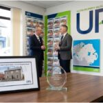 A framed Ulster Property Sales (UPS) listing document and award on a wooden desk in a professional Northern Ireland office.