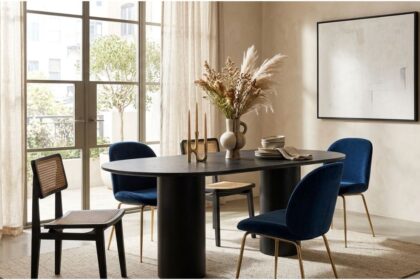 Black BD Studio Belle oval dining table styled with a ceramic vase and candles surrounded by blue velvet and cane chairs.