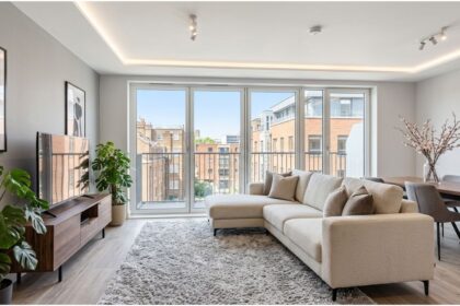 homes london rent Modern style ka ek London apartment jise rent par liya ja sakta hai. Isme ek open-plan living aur dining area hai jisme comfortable L-shaped beige sofa, ek media console, aur ek dining table rakhi hai.