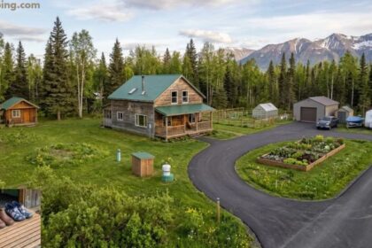 Farmhouse Properties showcasing a wooden country home with a green roof, landscaped garden, winding driveway, and scenic mountain views.